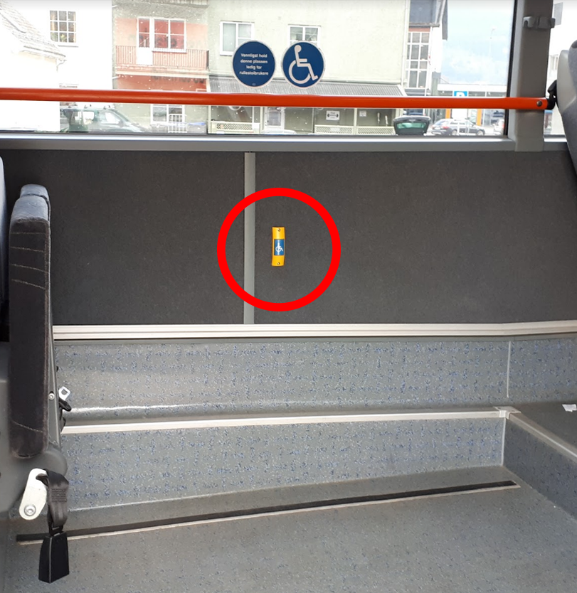 Bildet viser blå knapp med rullestol-symbol inne i bussen på motsatt side av den bakre inngangen. Knappen kan benyttes for å signalisere for sjåføren at man trenger lengere tid. 