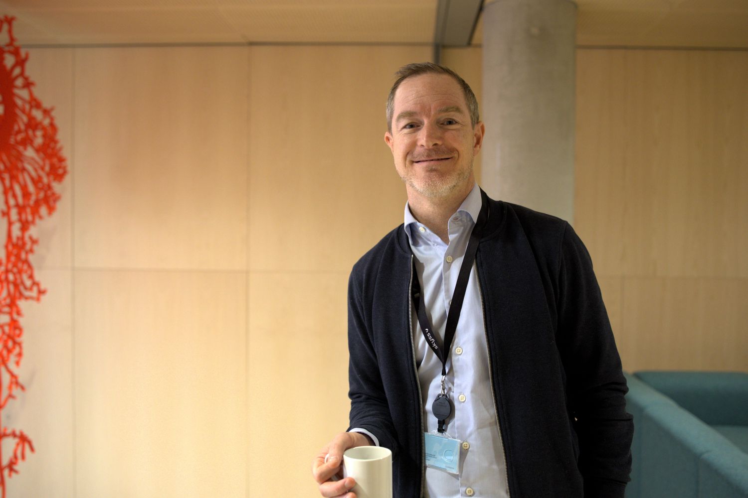 Bilete syner Daniel Michel Nilssen på Vestlandshuset med ein kaffikopp i handa medan han smiler